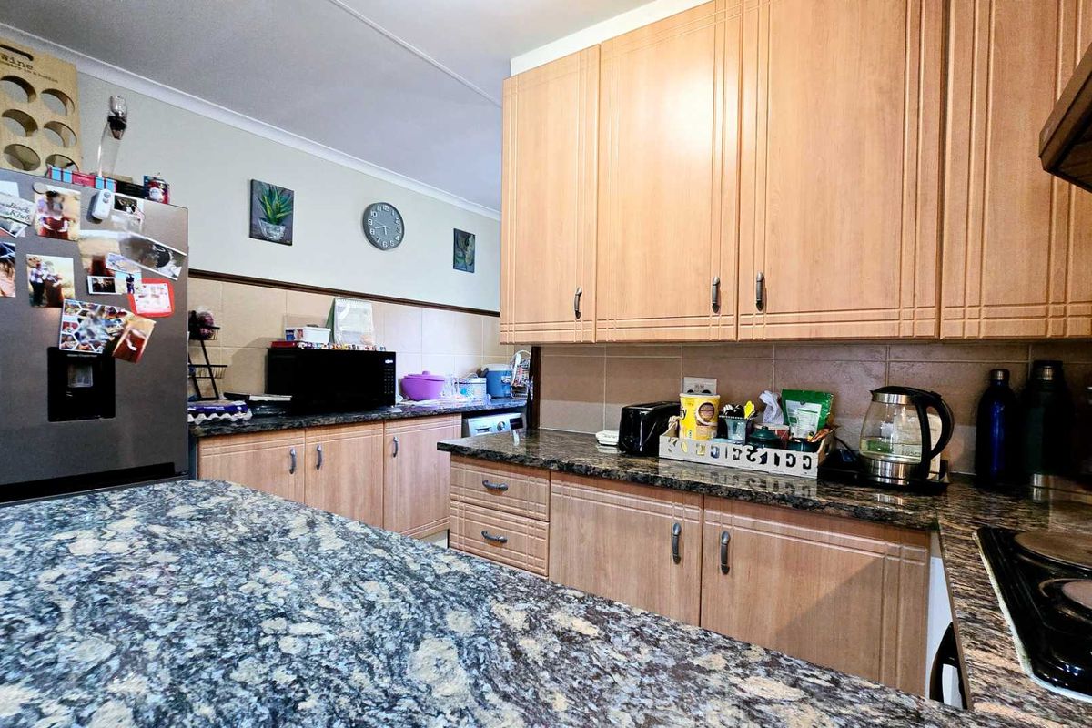 A functional kitchen featuring light wood-finish cabinetry, granite countertops, and a built-in hob with an extractor fan.