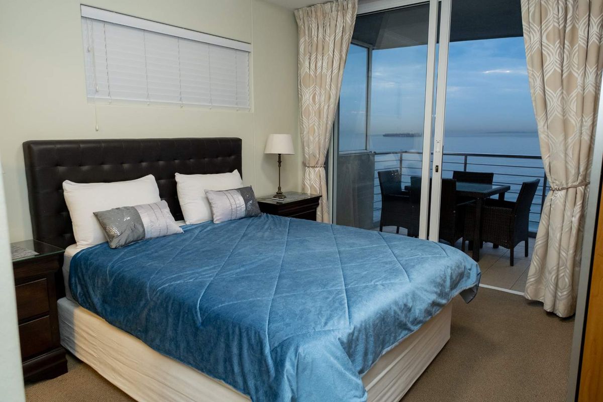 A well-maintained bedroom featuring carpet flooring and a large sliding glass door that opens onto a balcony with scenic water views.