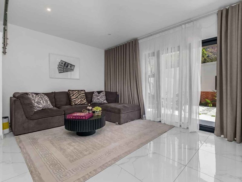 A bright and modern living room featuring polished marble-look floor tiles, recessed lighting, and large sliding glass doors providing access to the outdoor area.