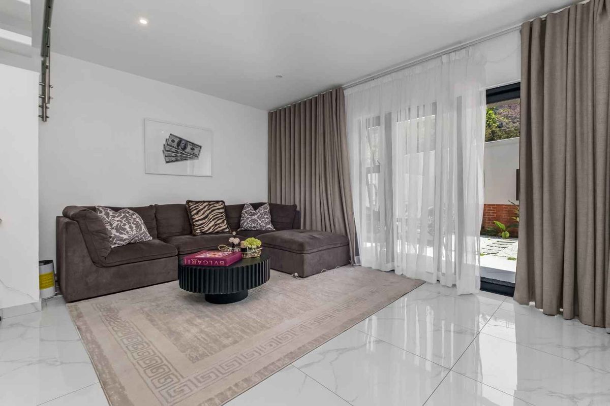 A bright and modern living room featuring polished marble-look floor tiles, recessed lighting, and large sliding glass doors providing access to the outdoor area.