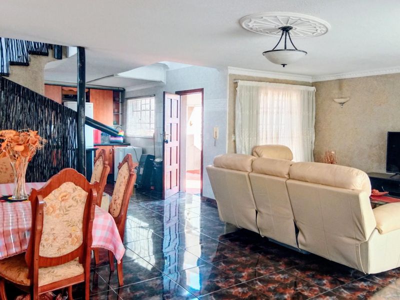 Open plan living and dining area featuring dark tiled flooring, a decorative ceiling rose, and a spiral staircase leading to the upper level.