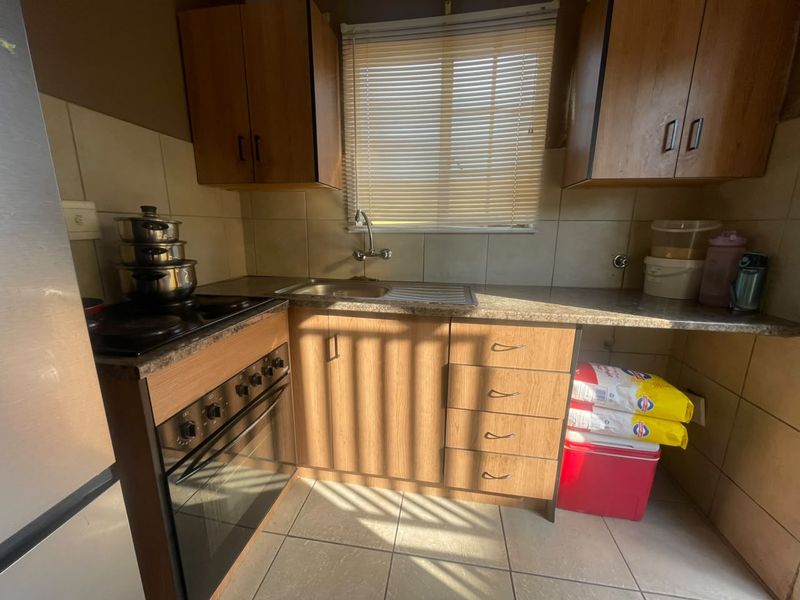 A functional kitchen featuring laminate cabinetry, tiled backsplash, built-in oven with hob, and a stainless steel sink with tiled flooring.
