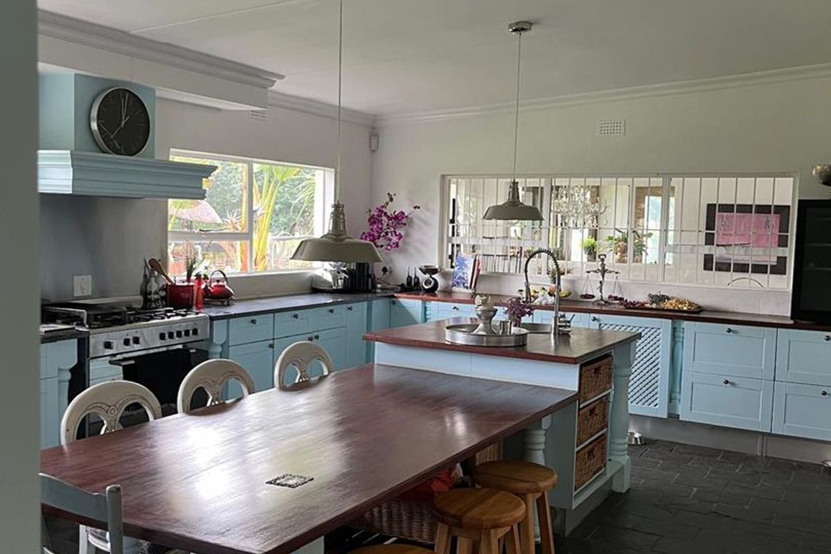 Spacious kitchen featuring light blue cabinetry, dark wood countertops, a central island with integrated dining table, and dark slate flooring.