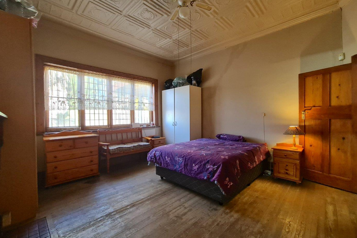 Spacious bedroom featuring a decorative pressed metal ceiling, large leadlight-style windows, and original timber flooring.