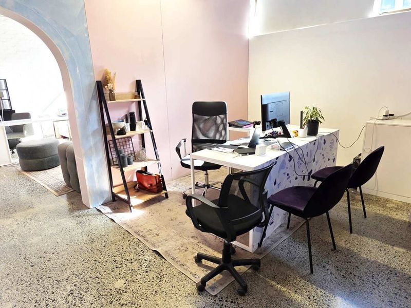 A bright office space featuring polished concrete floors and a distinctive arched entryway connecting to an adjacent workspace.