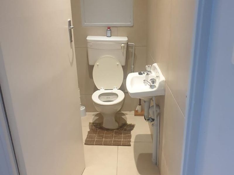 A compact guest bathroom featuring a toilet, wall-mounted basin, and neutral floor-to-ceiling tiling.