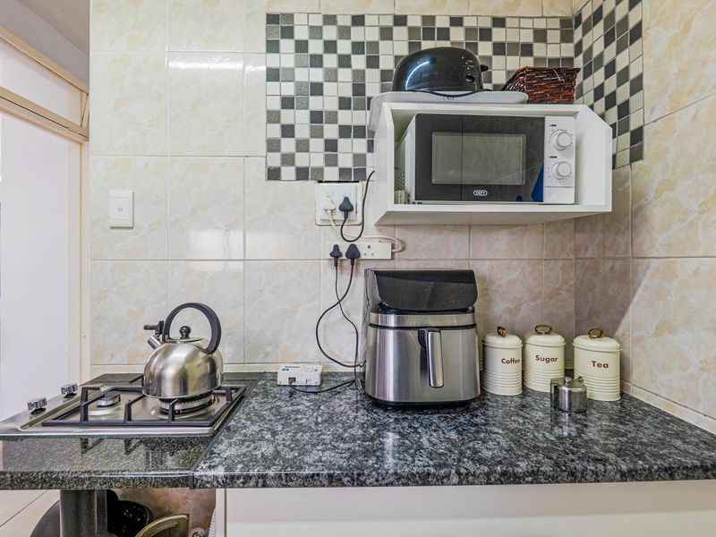 Compact kitchen area featuring a granite countertop, gas hob, and tiled backsplash with a dedicated built-in microwave shelf.