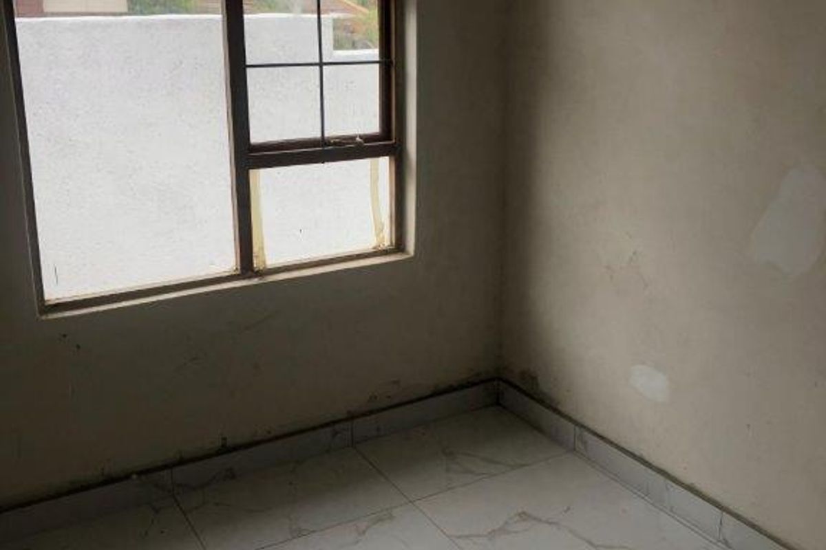 A small, unfinished bedroom featuring white marble-look floor tiles and a large window with a metal security frame.