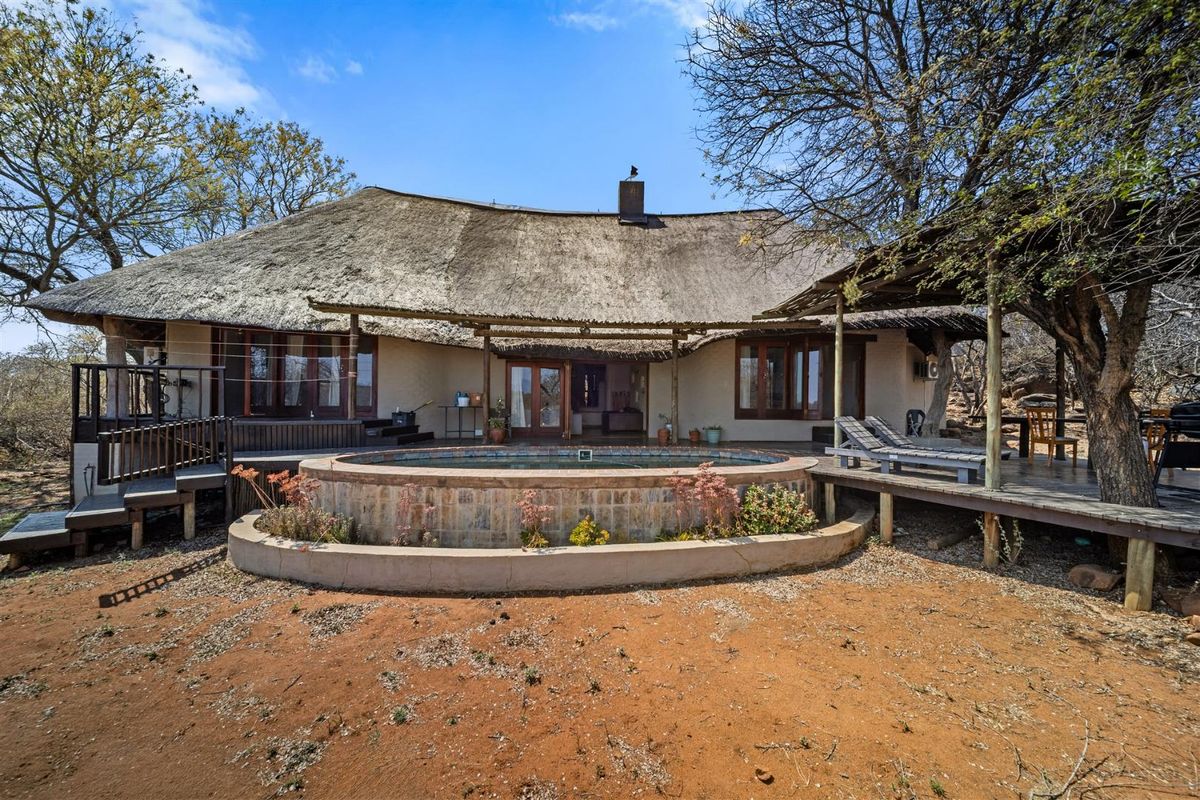 Rear view of a rustic home featuring a thatched roof, raised wooden deck, and a circular plunge pool set in a natural bushveld environment.
