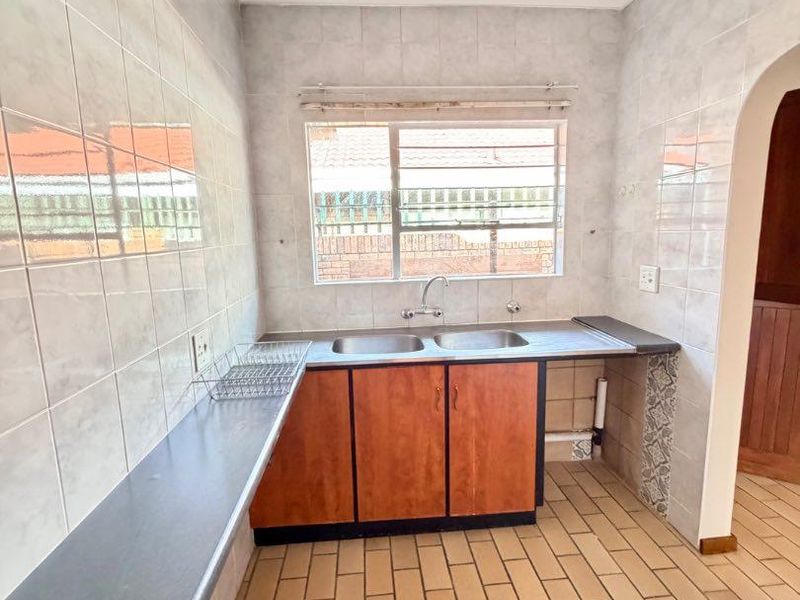 A functional scullery area featuring a double stainless steel sink, laminate countertops, tiled splashbacks, and tiled flooring.