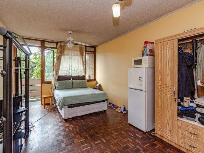 A bedroom featuring parquet flooring, a ceiling fan, and access to a balcony through sliding glass doors.