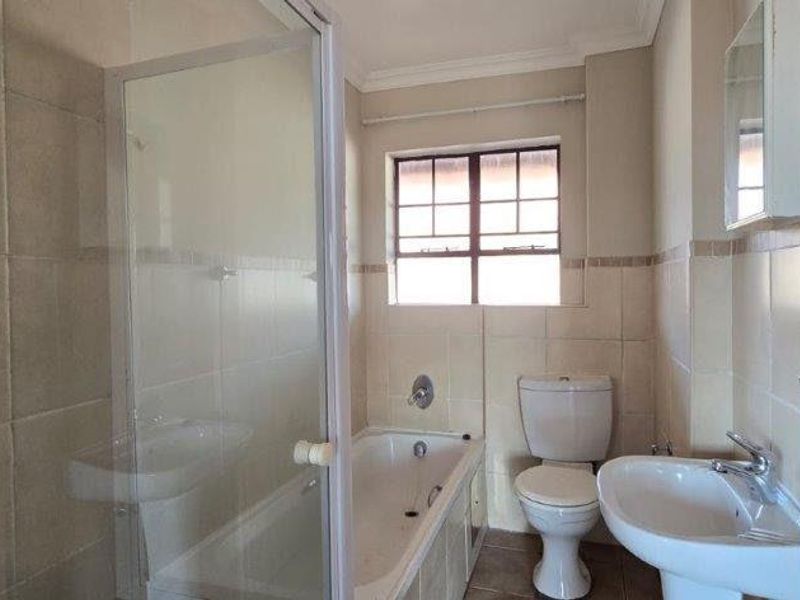 A functional bathroom featuring a shower enclosure, bathtub, pedestal basin, and toilet with neutral wall and floor tiling.