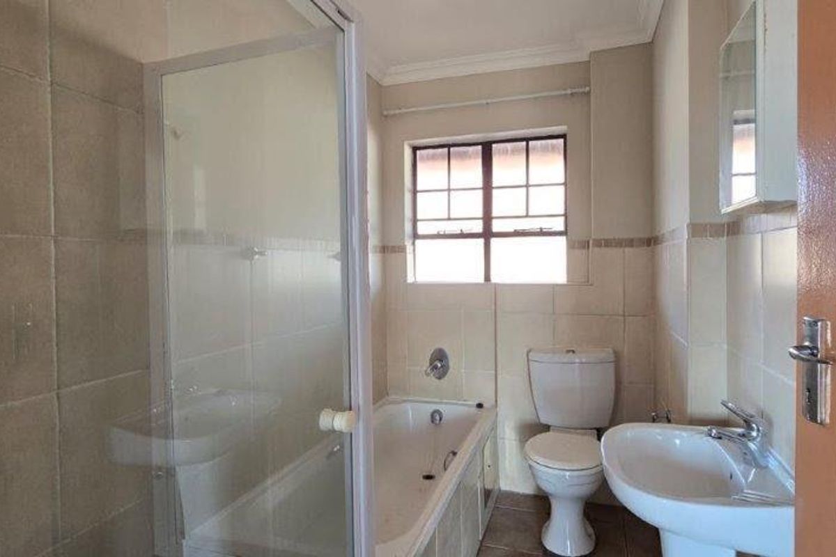 A functional bathroom featuring a shower enclosure, bathtub, pedestal basin, and toilet with neutral wall and floor tiling.