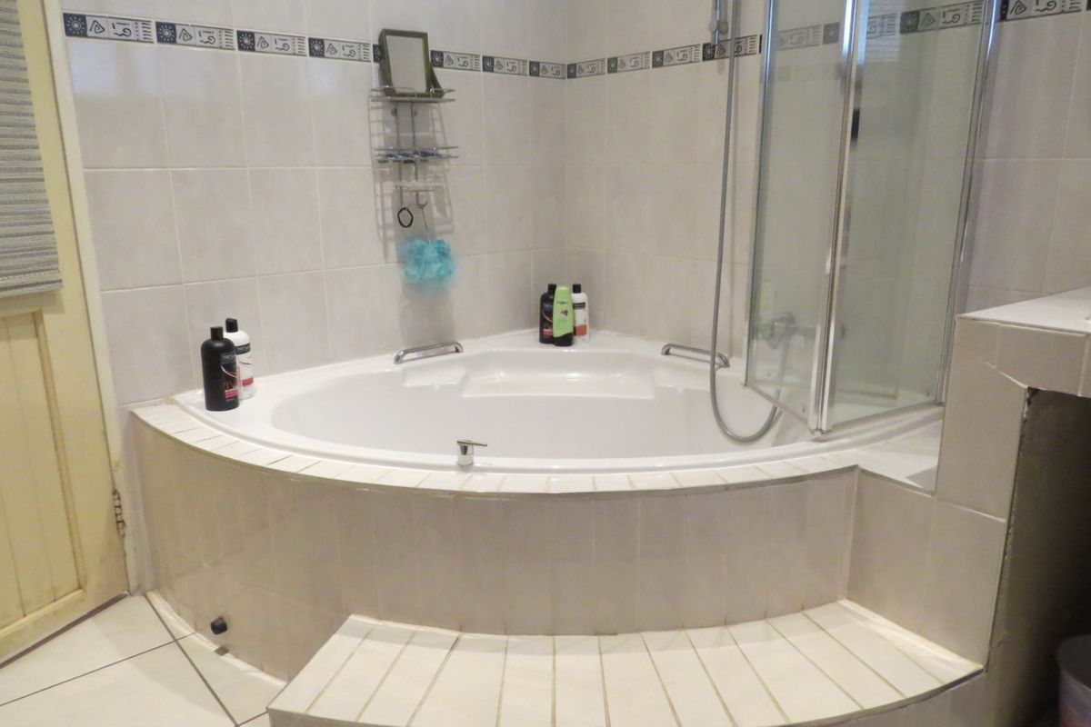 A bathroom featuring a corner bathtub with integrated shower, tiled surround, and decorative border tiles.