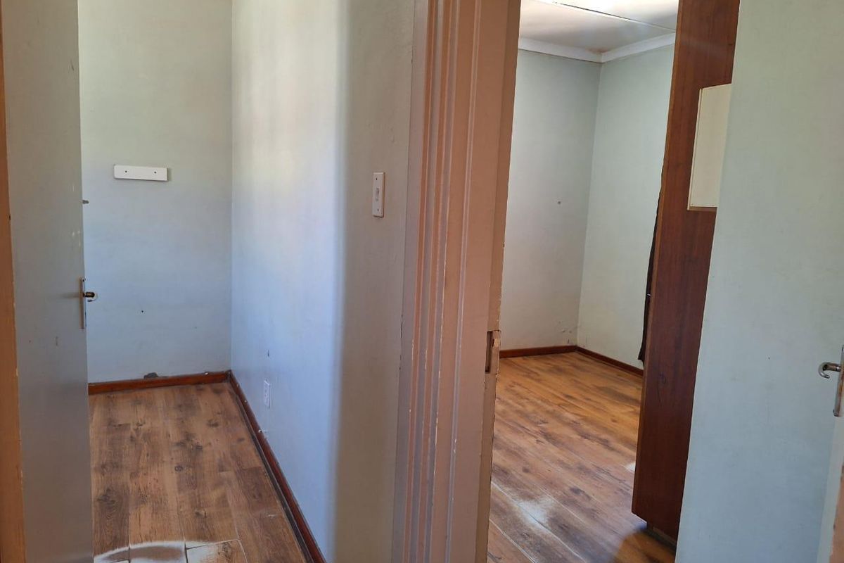 A view through a doorway into an empty bedroom featuring wood-look laminate flooring and plain painted walls.