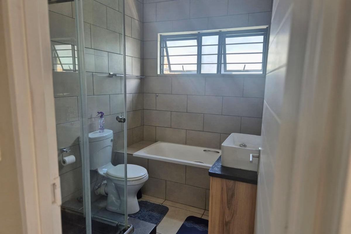 A modern bathroom featuring a glass-enclosed shower, a built-in bathtub, a vanity with a vessel sink, and neutral wall tiling.