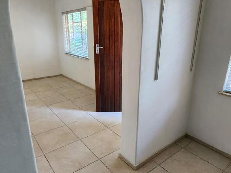 A bright, empty hallway featuring ceramic floor tiles, an arched doorway leading to an adjacent room, and a solid wooden door.