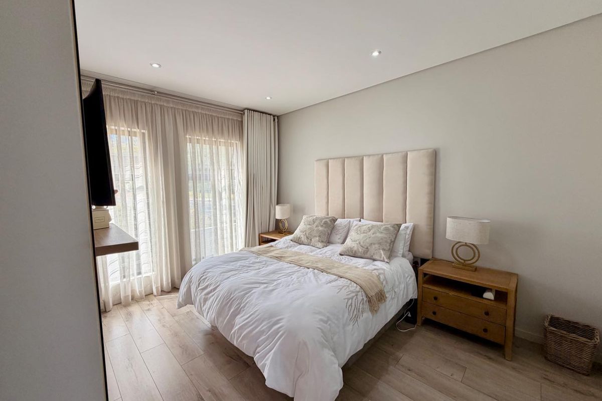 A well-maintained bedroom featuring modern laminate flooring, recessed downlighting, and floor-to-ceiling curtains providing access to natural light.