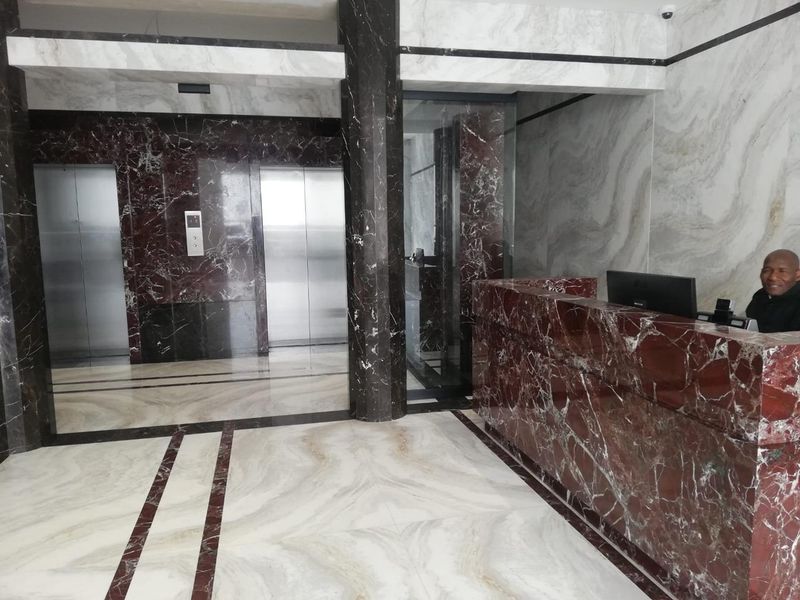 Modern office building lobby featuring high-end marble wall and floor finishes, a built-in reception desk, and a professional elevator bank.