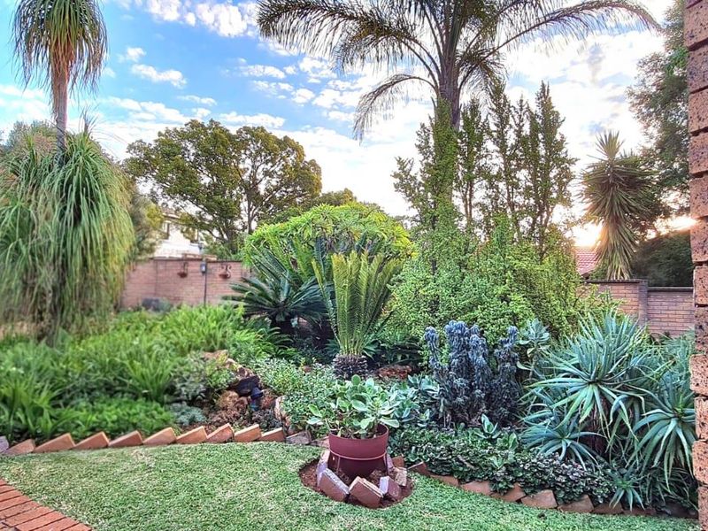 A well-maintained front garden featuring established landscaping, brick paving, and a secure perimeter wall with a metal gate.