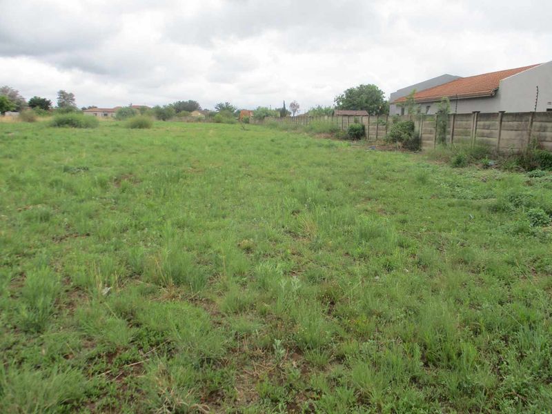 A vacant residential plot featuring grass cover and a precast concrete boundary wall along the side perimeter.