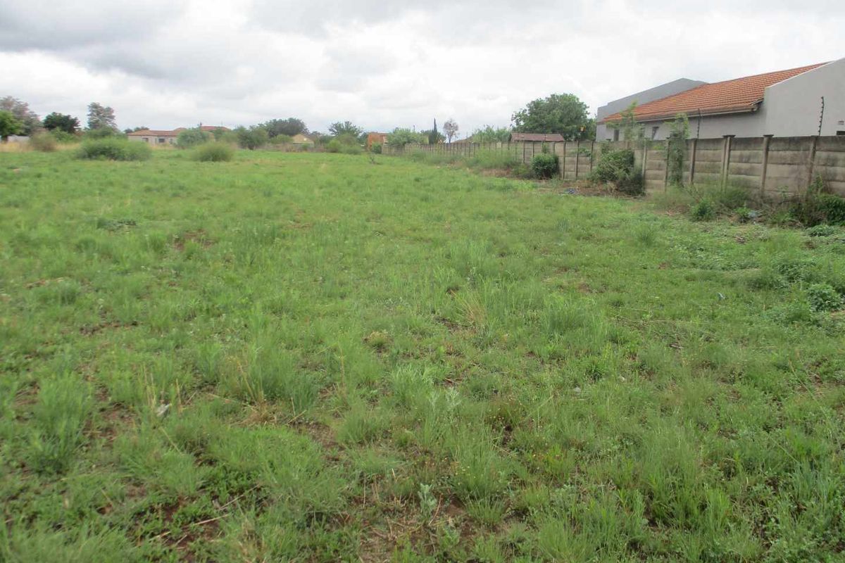 A vacant residential plot featuring grass cover and a precast concrete boundary wall along the side perimeter.