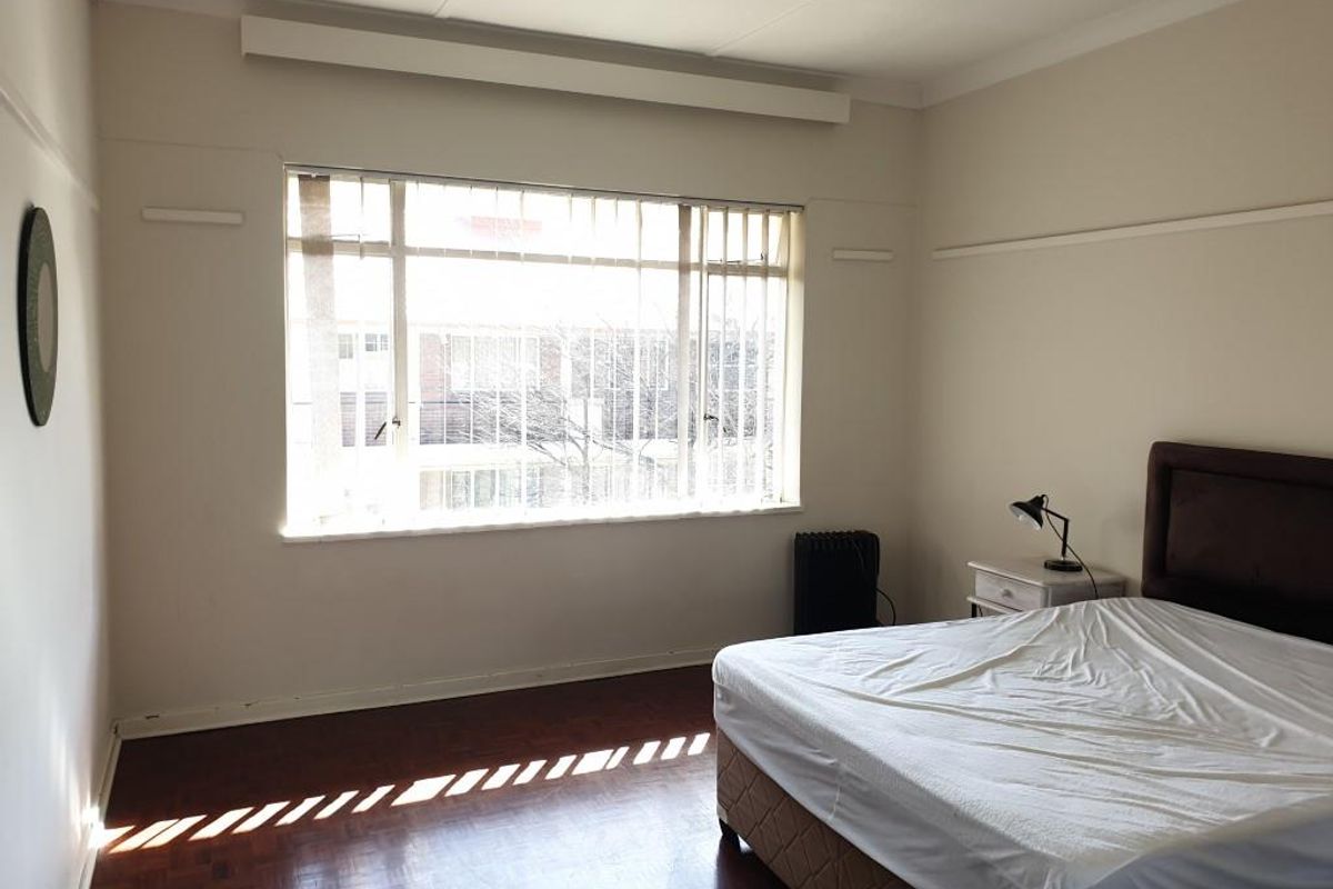 A spacious bedroom featuring original parquet flooring, large window with vertical blinds, and picture rails.
