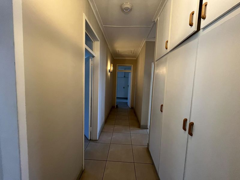 A clean, functional hallway featuring neutral tiled flooring and extensive built-in storage cupboards along one side.