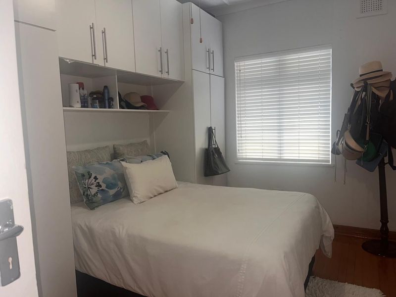 A compact bedroom featuring white built-in cabinetry, timber flooring, and a window fitted with venetian blinds.