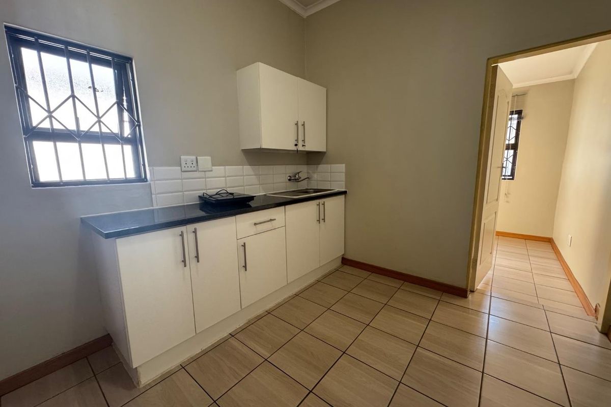 A compact kitchen area featuring white built-in cabinetry, a dark laminate countertop, stainless steel sink, and neutral ceramic floor tiles.