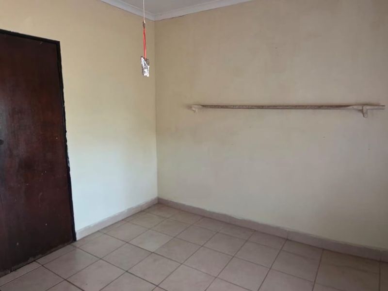 An empty bedroom featuring tiled flooring and a built-in wooden cupboard, presenting a blank canvas for renovation or interior design updates.