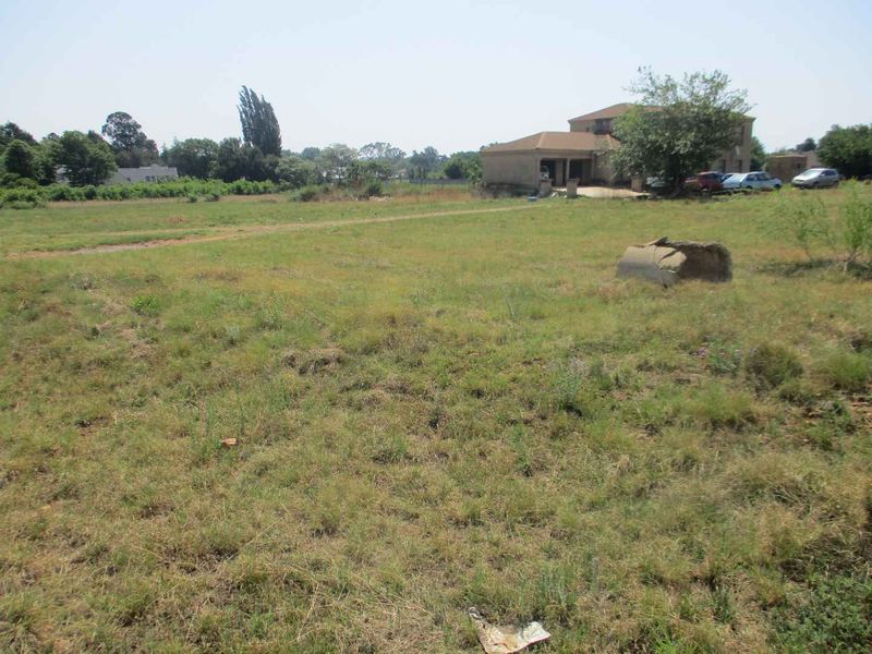A wide-angle view of a vacant residential plot featuring open grassland with a neighboring property visible in the background.
