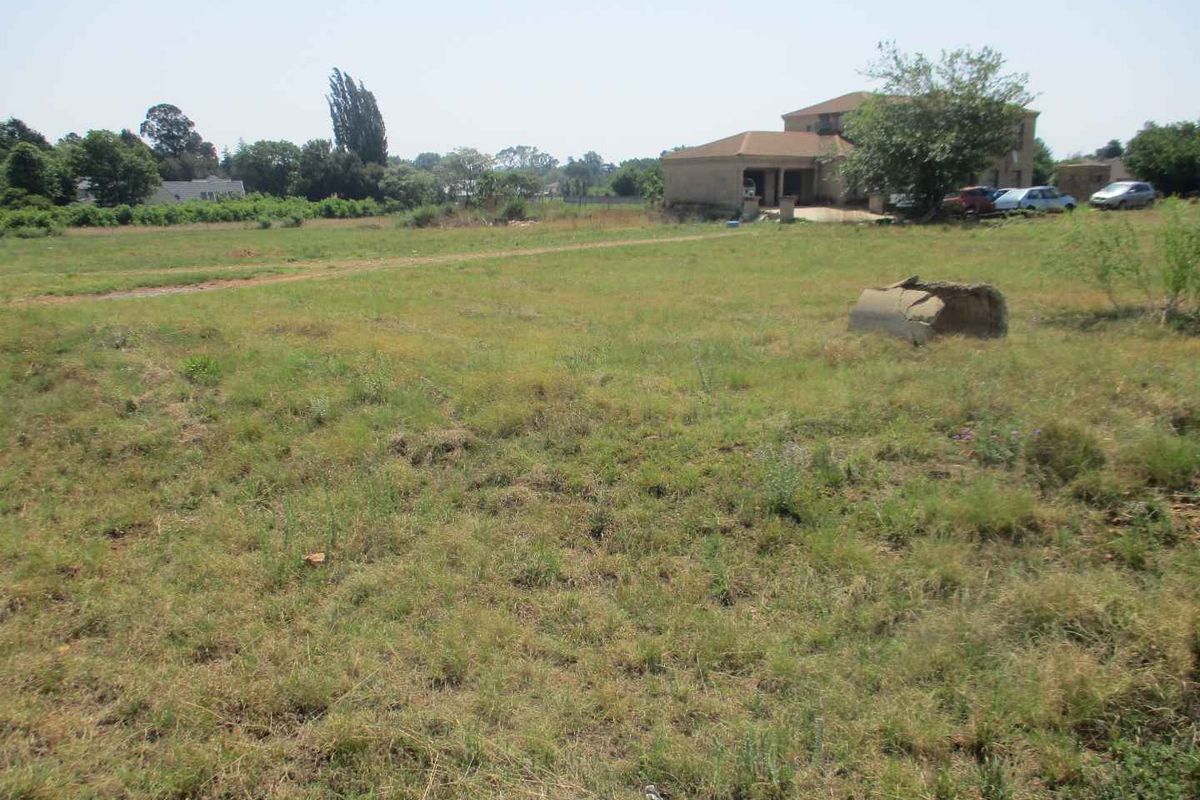 A wide-angle view of a vacant residential plot featuring open grassland with a neighboring property visible in the background.