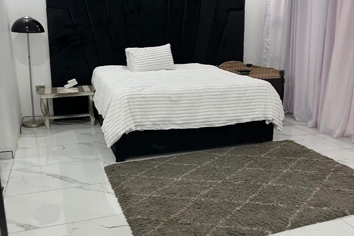 A modern bedroom featuring large-format marble-look floor tiles, recessed ceiling lighting, and a prominent built-in black headboard.