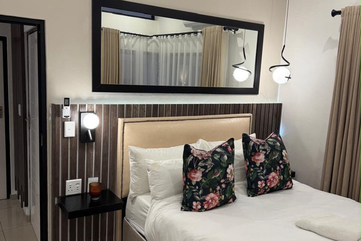 A well-maintained bedroom featuring a modern built-in headboard with integrated accent paneling, stylish pendant lighting, and neutral tiled flooring.