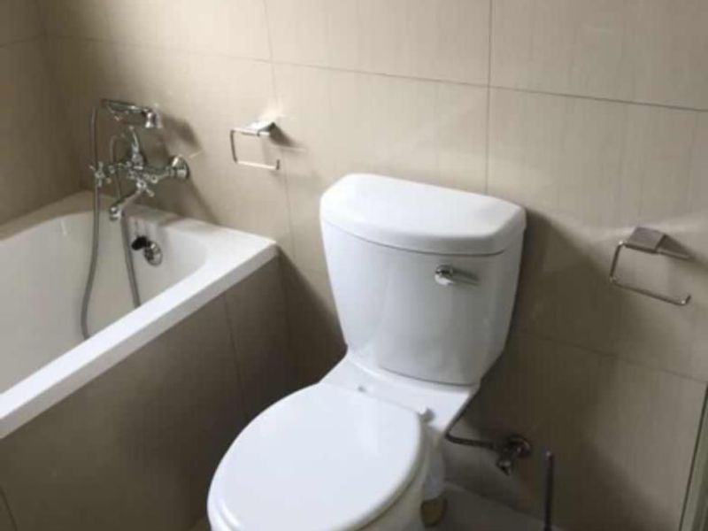 A functional bathroom featuring a bathtub, toilet, and neutral ceramic wall and floor tiling.
