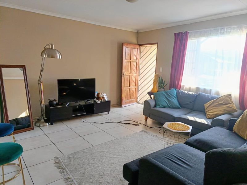 A living room featuring tiled flooring, a wooden entrance door, and a large window allowing natural light into the space.