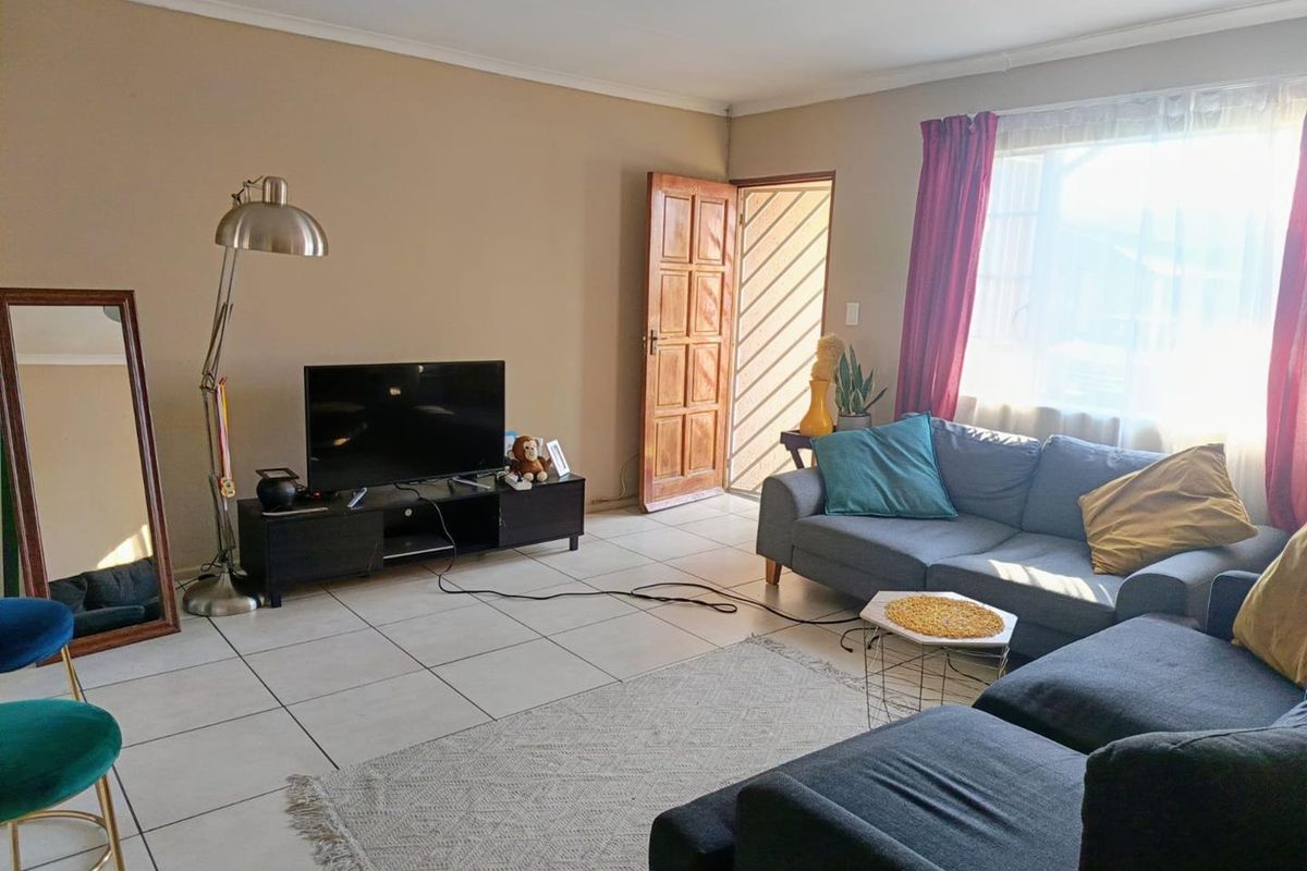 A living room featuring tiled flooring, a wooden entrance door, and a large window allowing natural light into the space.
