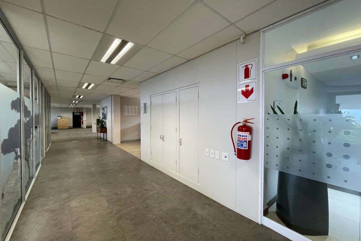 A clean, well-lit office hallway featuring a suspended ceiling, glass partitions, and integrated fire safety equipment.