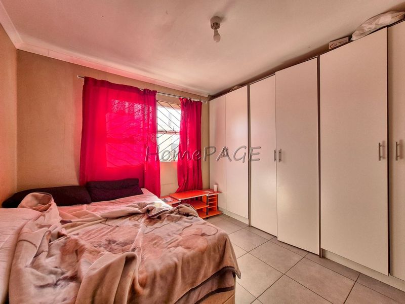 A bedroom featuring tiled flooring, built-in cupboards, and security bars on the window.