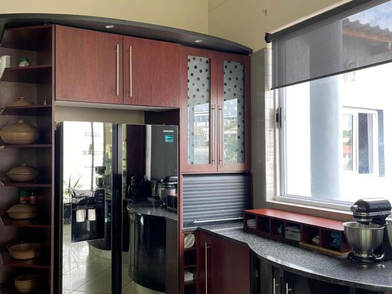 A modern kitchen featuring dark wood and black cabinetry, granite countertops, tiled flooring, and an integrated appliance garage with a roller shutter.