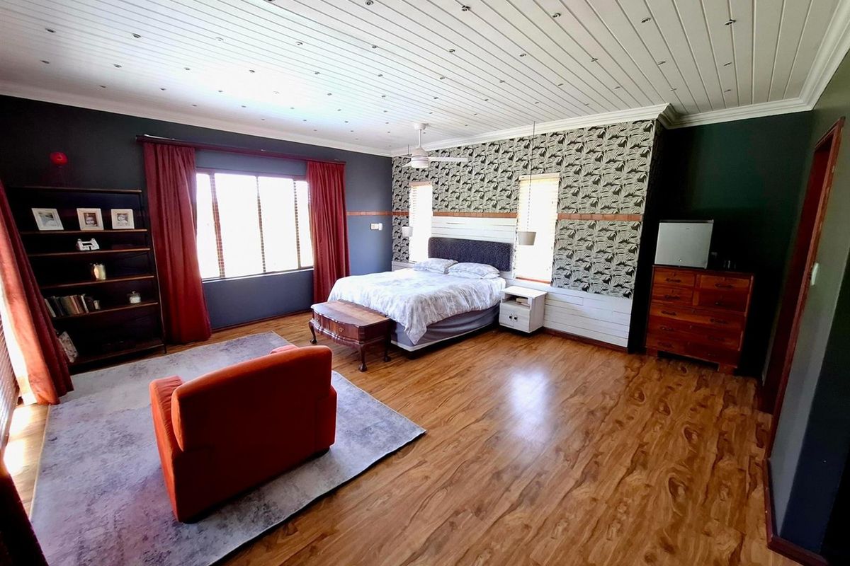 Spacious bedroom featuring timber laminate flooring, a tongue and groove ceiling with a central fan, and decorative wall panelling.