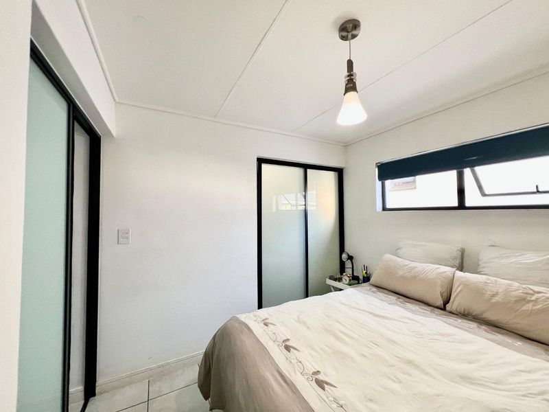 A well-maintained bedroom featuring tiled flooring, built-in sliding door cupboards, and a top-hung window providing natural light.