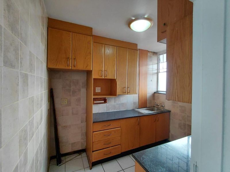 A functional kitchen featuring wooden cabinetry, laminate countertops, a stainless steel sink, and tiled finishes throughout.