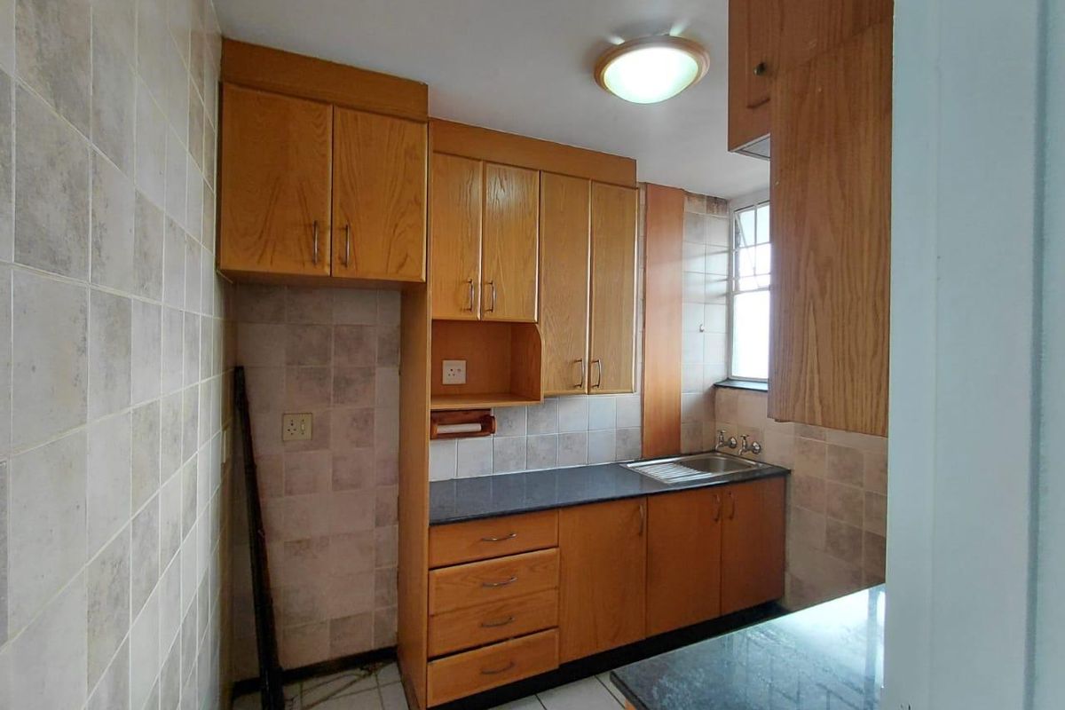 A functional kitchen featuring wooden cabinetry, laminate countertops, a stainless steel sink, and tiled finishes throughout.