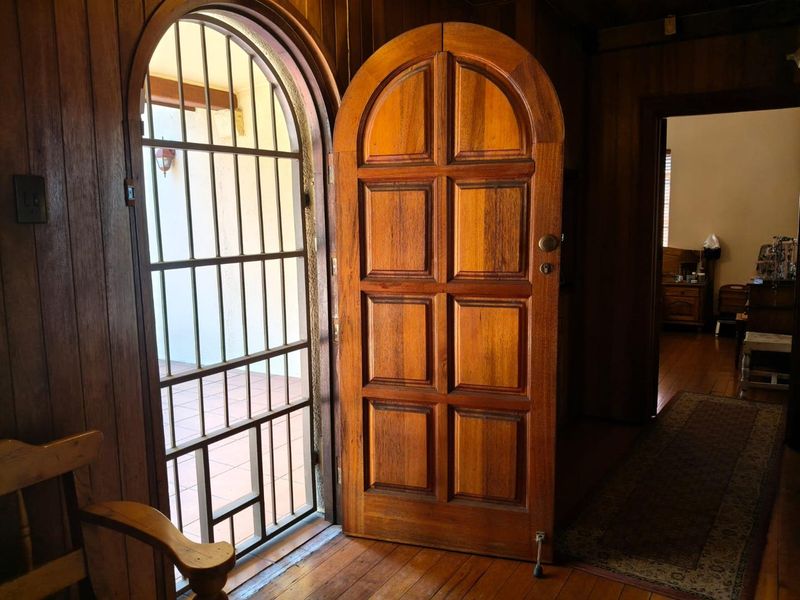 An inviting entryway featuring classic timber wall paneling, polished wooden floors, and a distinctive arched solid timber door with an integrated security gate.