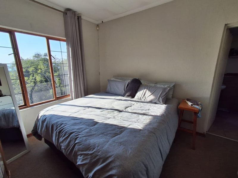 A bedroom featuring a large window with natural light, carpeted flooring, and neutral wall finishes, offering a functional space for rest.