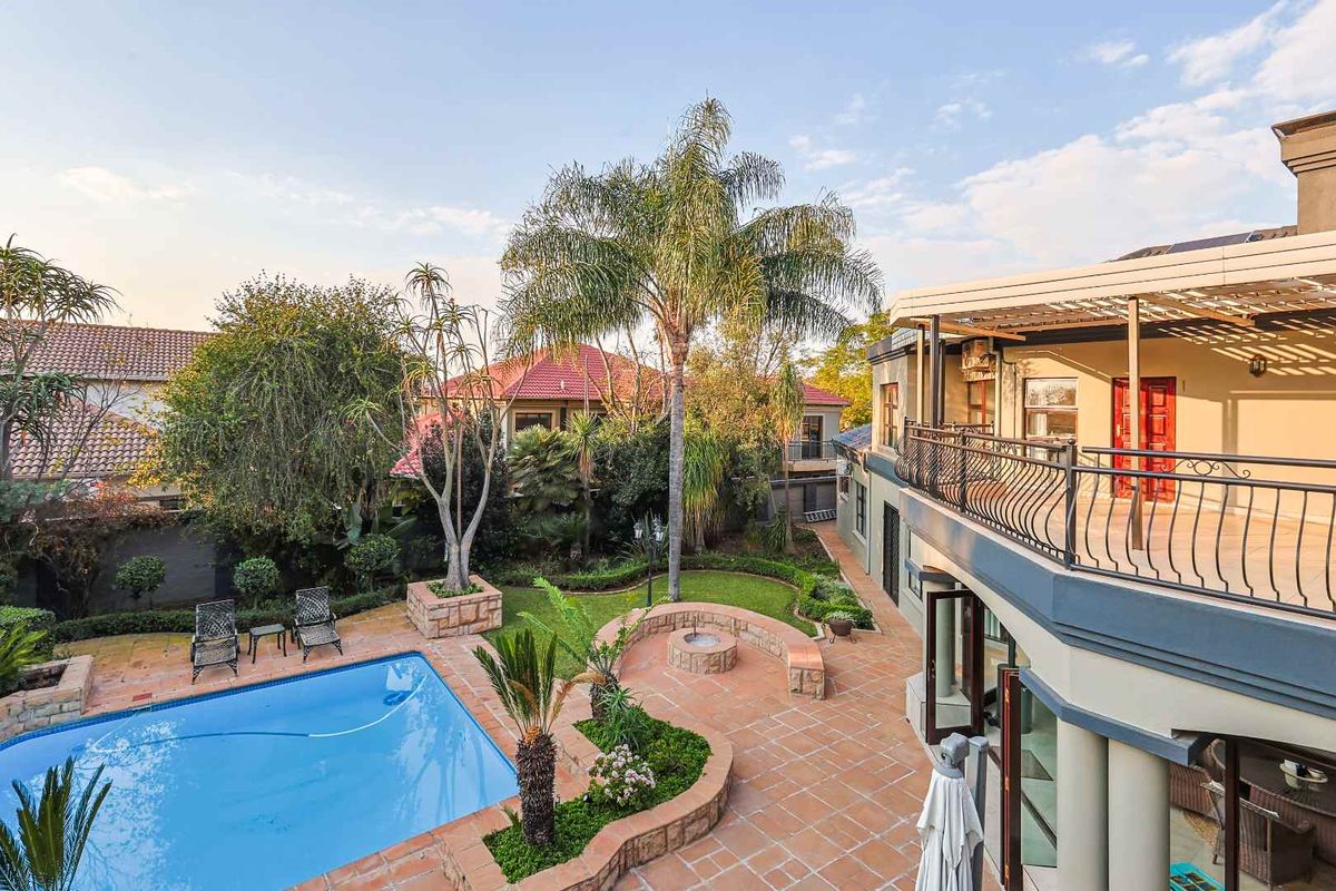 Spacious rear exterior featuring a swimming pool, landscaped garden, paved patio area, and an elevated balcony with wrought iron railings.