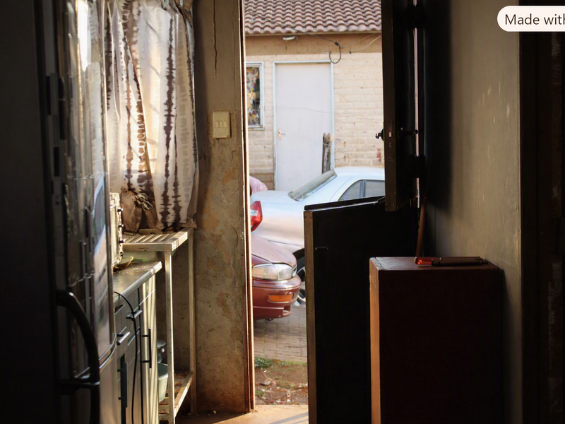 A view from an interior kitchen space looking out through an open doorway toward a driveway and exterior building facade.