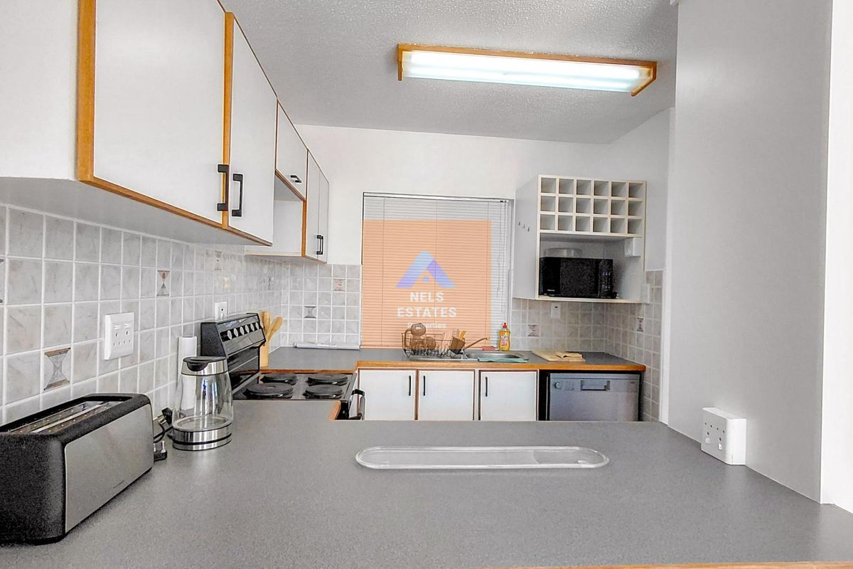 A functional kitchen featuring white cabinetry, laminate countertops, tiled backsplash, and an integrated electric stove with overhead lighting.